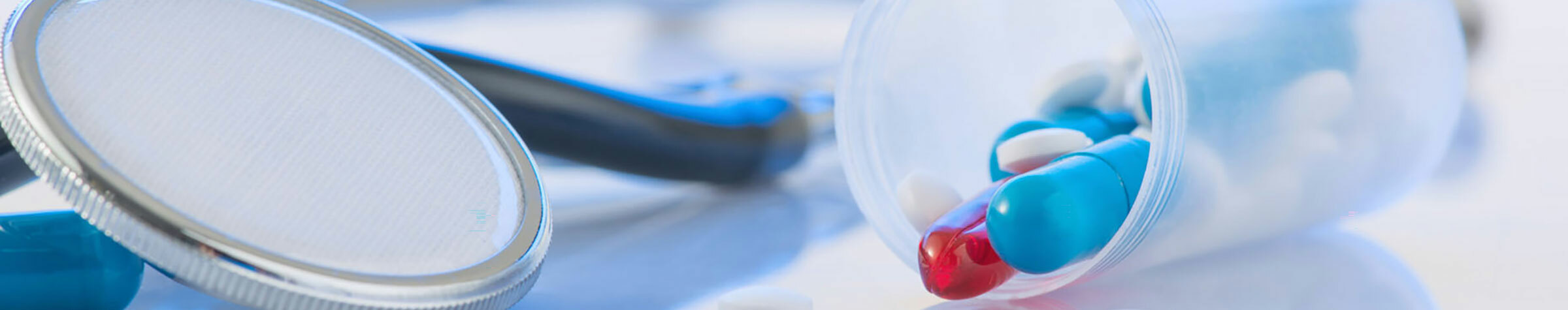 Blue stethoscope on a white surface next to a pill bottle with blue, white and red pills
