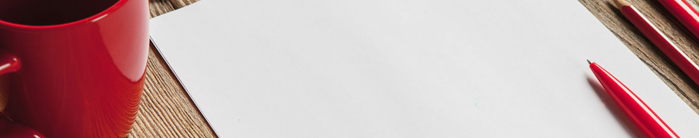 Red coffee cup next to a blank sheet of paper and three red pens