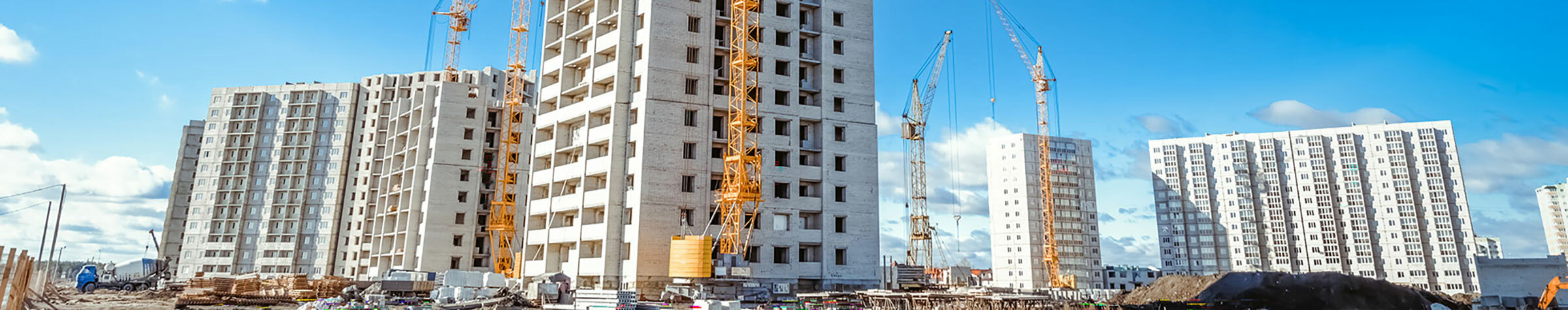 Several concrete high rise buildings on a construction site with yellow cranes